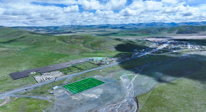 Aerial view of a solar PV microgrid next to a remote high-altitude village, with grasslands and mountains around it
