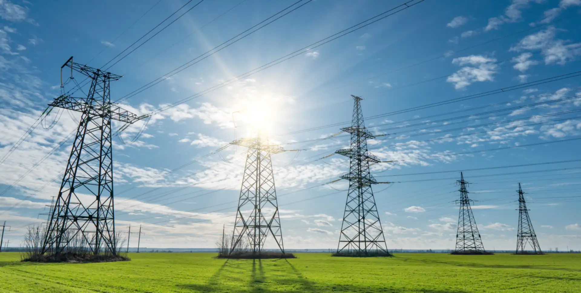 Power transmission towers across green fields under a bright sun