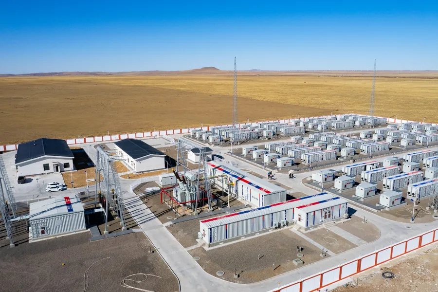 Rows of prefabricated battery storage and E-House modules at a renewable energy site on open grassland