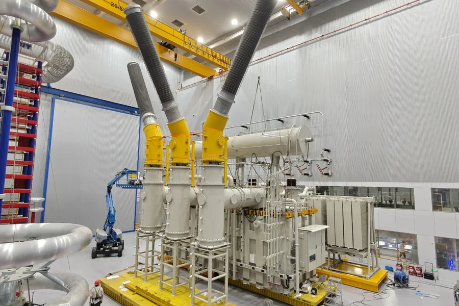 Large power transformer with yellow high-voltage bushings in a factory test hall