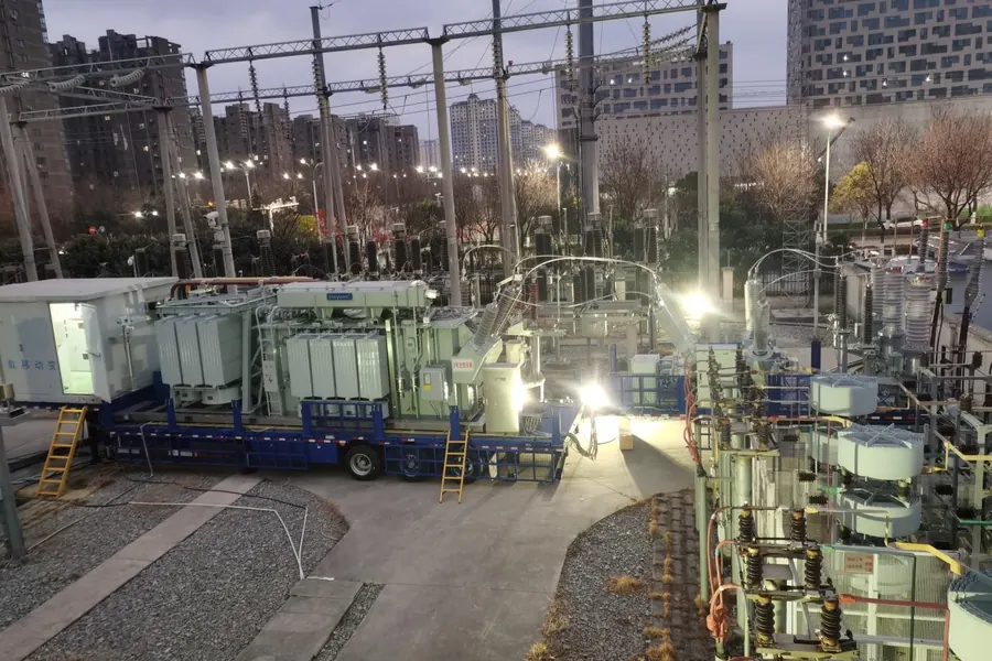 Mobile substation operating at dusk beside existing substation equipment in a city